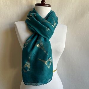 Teal scarf featuring a gold-foiled Eiffel Tower pattern and the text "Paris”